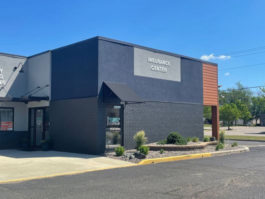 Modern commercial building exterior with dark gray facade, brick accent, and parking lot under clear blue sky