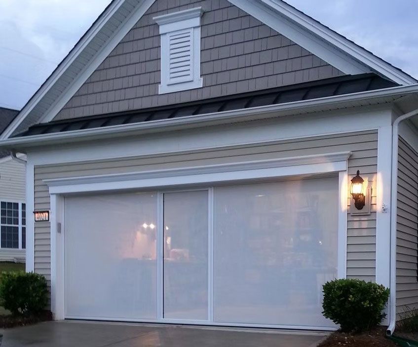 A garage door opening featuring a white, retractable mesh screen covering the entrance of a house.
