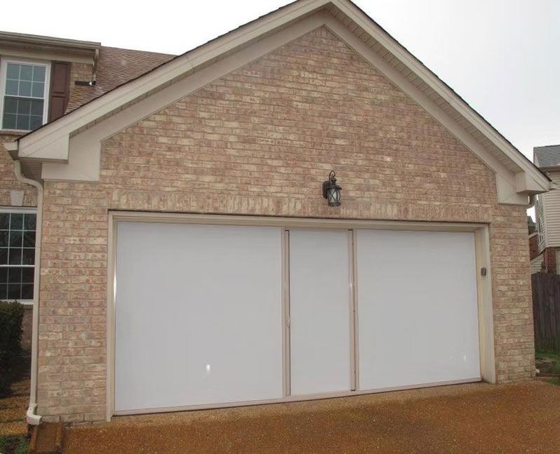 A beige brick house exterior featuring a wide, white, three-panel garage door under a gabled roof.