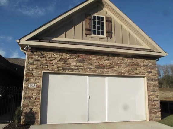 A garage with stone facade, white doors, and a small attic window under a gabled roof against a blue sky.