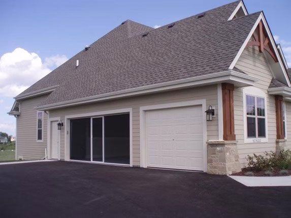 A tan suburban house with a two-car garage, one bay open with a screen and the other closed, under a clear blue sky.