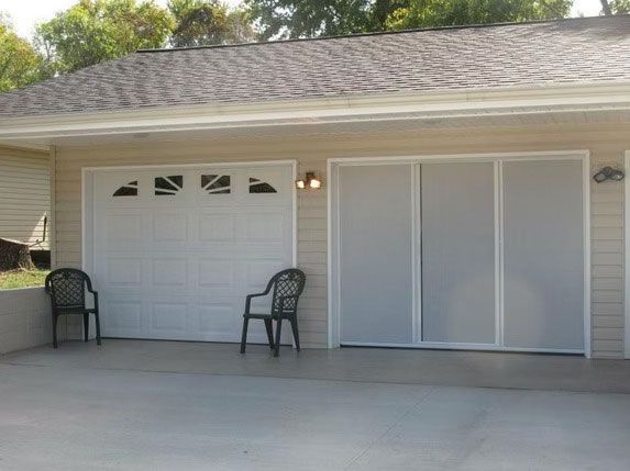 A garage with a white sectional door and a set of sliding glass doors, with two chairs sitting on the concrete driveway.
