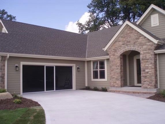 A beige suburban home with a stone entryway, gray roof, and a screened-in garage door opening onto a concrete driveway.