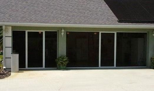 A patio area with dark-tinted glass sliding doors, white frames, a potted plant, and a gray shingled roof.