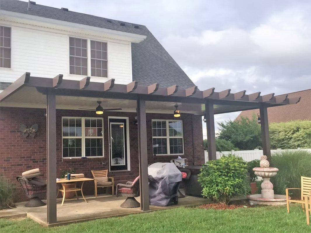 A patio with a brown wooden pergola over a concrete floor, featuring outdoor furniture, a grill, and a stone fountain.
