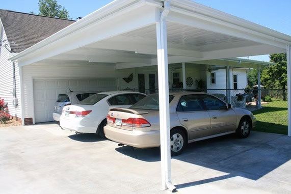 Two cars parked under a white carport attached to a suburban house on a sunny day.