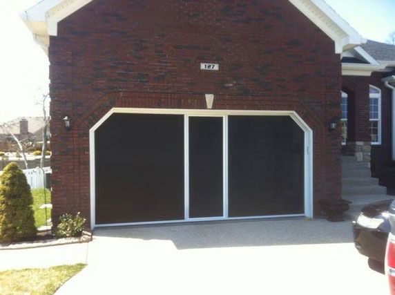 A brick house with a white-framed, retractable garage door screen covering the open garage bay.