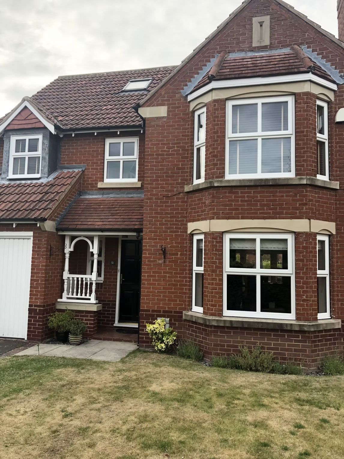 A two-story red brick house with white-framed windows, a covered front porch, and a brown tiled roof.