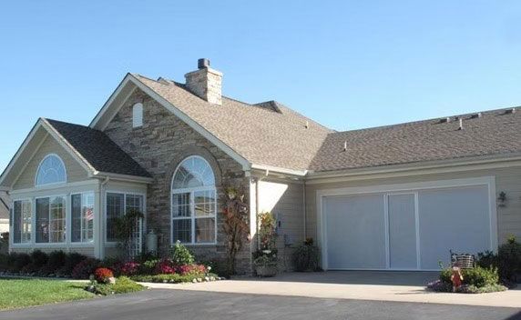 A one-story suburban house with a stone facade, a sunroom with many windows, a two-car garage, and a landscaped front yard.