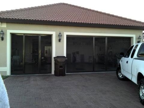 A house exterior with two large garage bays covered by dark screen doors, and a white pickup truck parked in the driveway.
