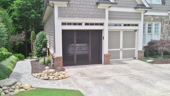 A two-car garage at a house with a screen door covering one bay, a stone walkway, and landscaped garden beds.