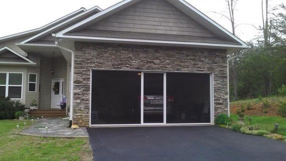 A suburban house with stone siding on the garage, which features a large, dark-screened door system.