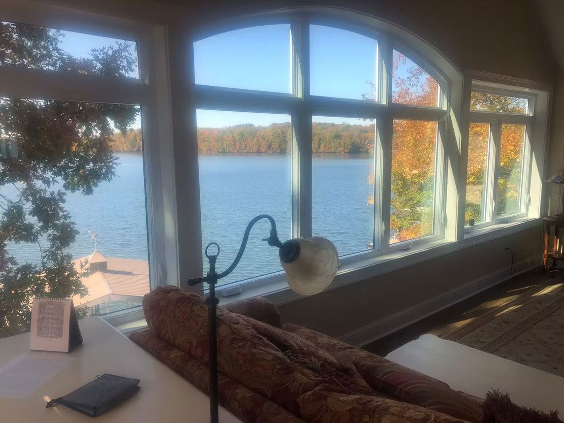 A bright room with a large arched window overlooking a blue lake surrounded by autumn trees.