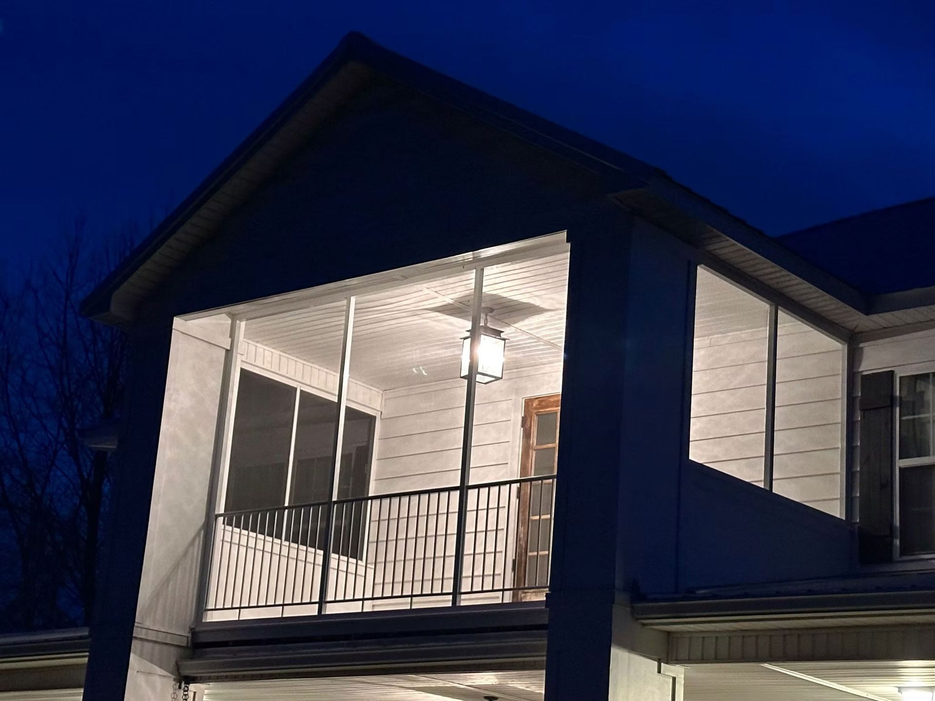 A well-lit, screened-in porch with a decorative metal railing at dusk, attached to a house with white siding.