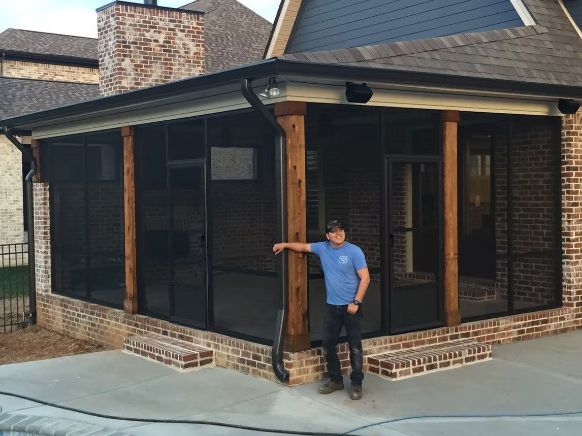 A person leans against a wooden post in front of a modern screened-in brick porch.