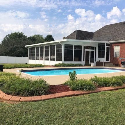 A swimming pool in a backyard with a large, white screen-enclosed patio attached to a red brick house under a blue sky.