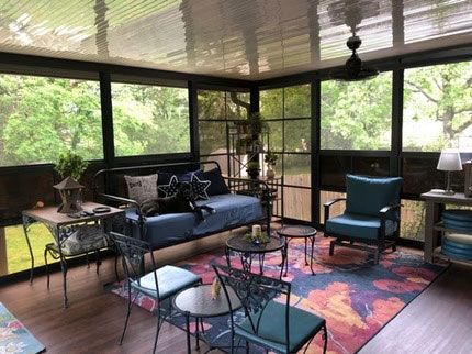 A furnished screened-in porch with a blue sofa, matching armchair, iron tables, and a colorful floral rug on a deck.