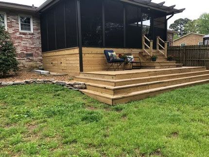 A newly built wooden deck with wide steps and a screened-in porch attached to the brick exterior of a house.