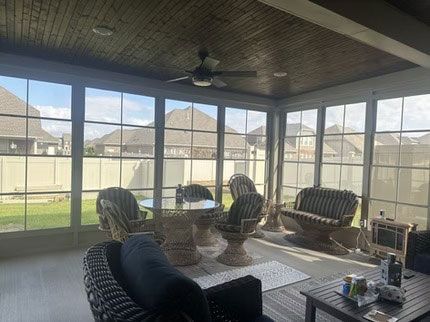 A sunroom with wicker furniture, a table, and a ceiling fan, overlooking a backyard through large paneled windows.