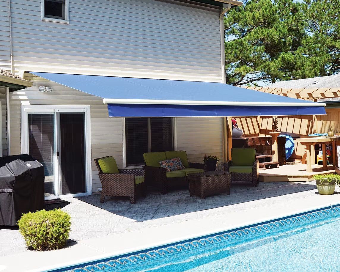 Blue retractable awning extended over a patio with wicker furniture next to a swimming pool.