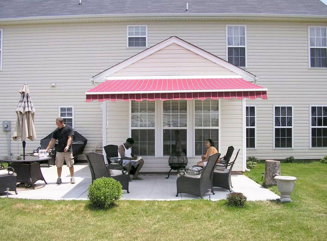 People relaxing on a backyard patio under a red and white striped retractable awning attached to a house.