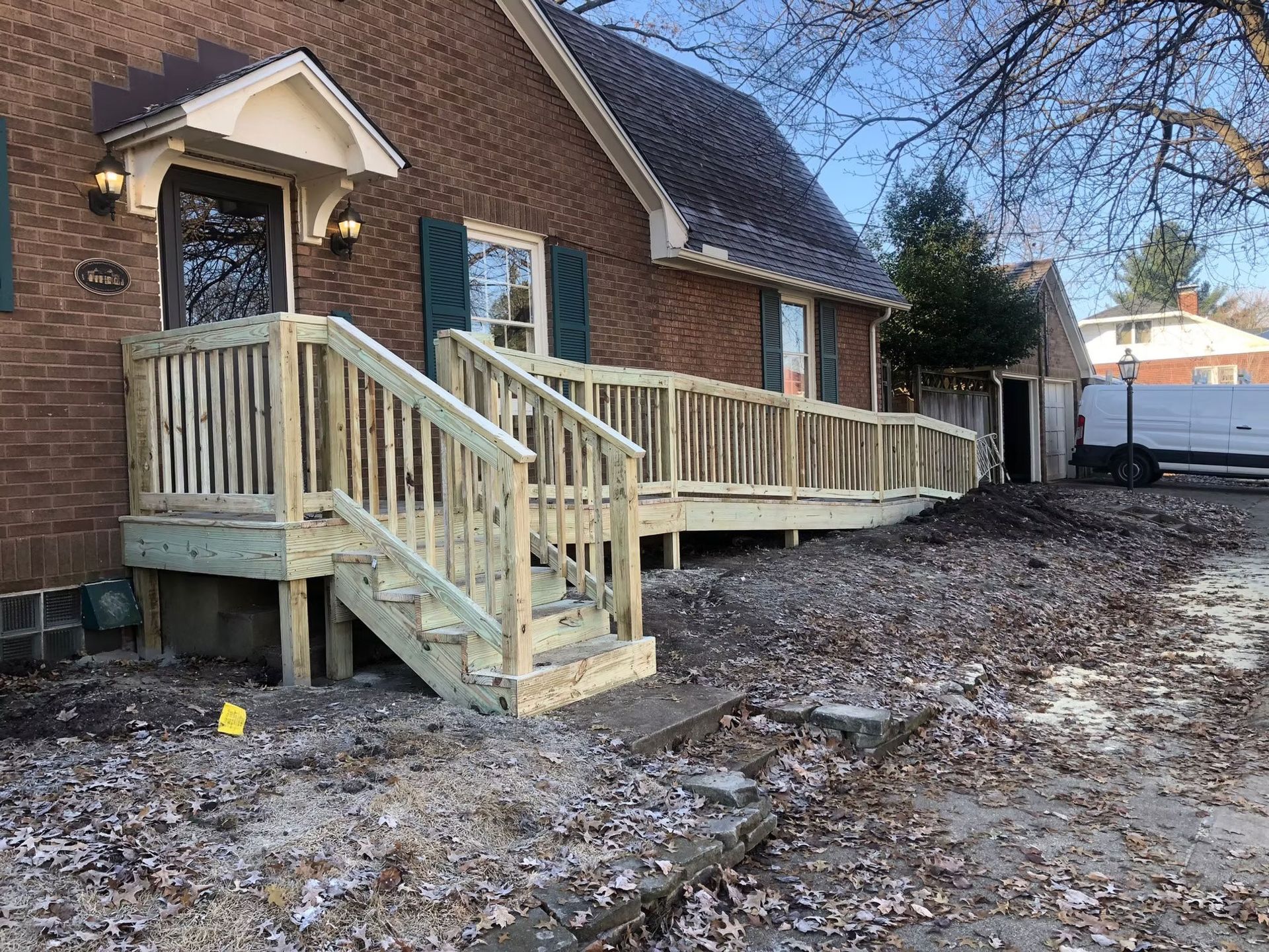A newly built wooden wheelchair ramp with stairs leading to the entrance of a brick house.