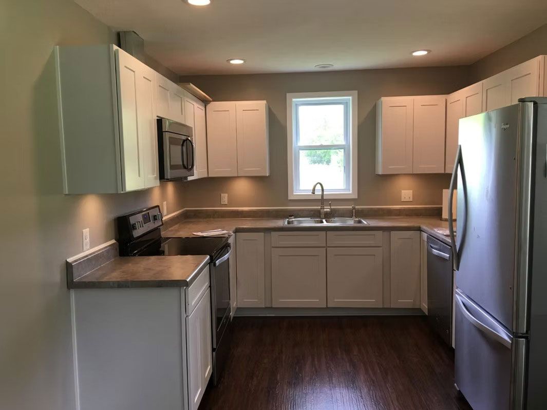 A modern kitchen featuring white cabinets, stainless steel appliances, dark wood floors, and a window above the sink.