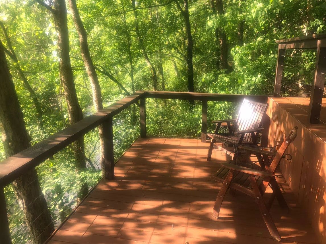 Two wooden deck chairs on a brown wooden deck overlooking a lush, green forest.