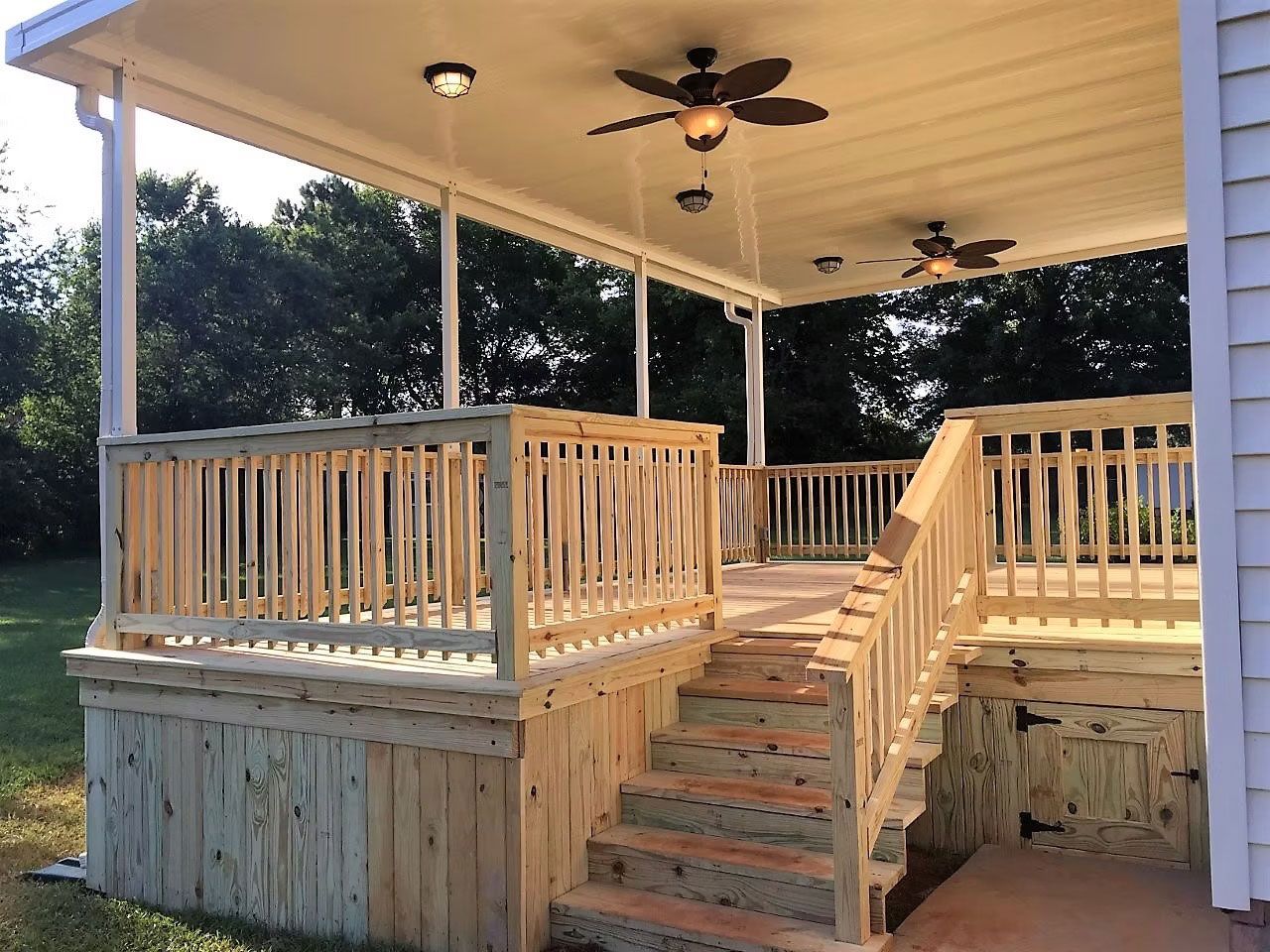 A newly built wooden deck with a covered patio area, ceiling fans, and a staircase leading to a grassy backyard.