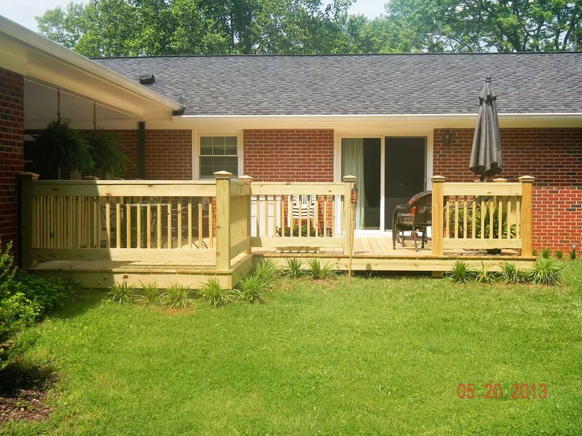 A newly built wooden deck attached to a brick house with a lawn in the foreground.