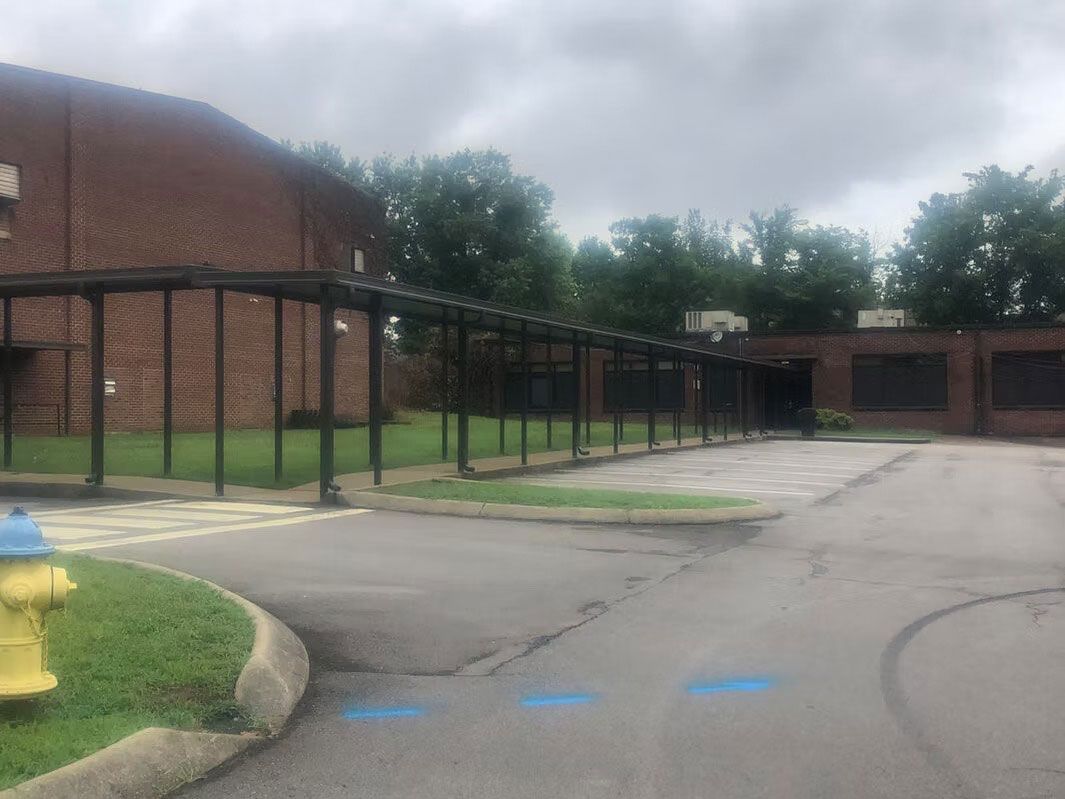 An outdoor covered walkway connects two brick buildings near a driveway with a yellow fire hydrant in the foreground.