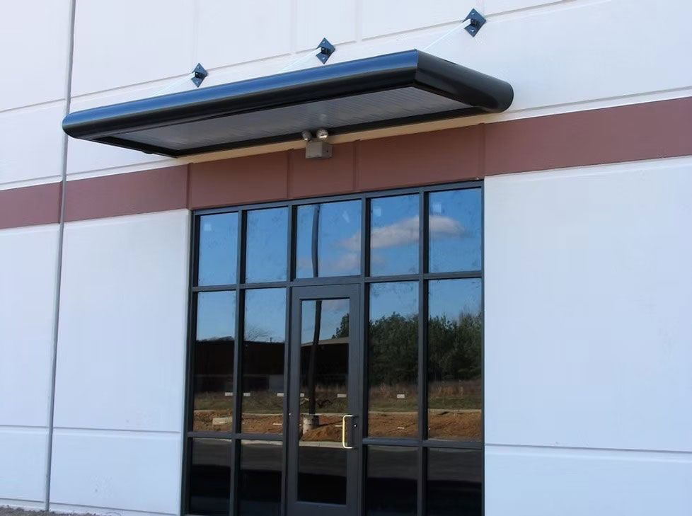 An exterior commercial entrance with glass double doors, a dark metal frame, and a horizontal black metal awning above.