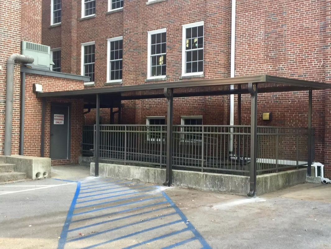 Brick building exterior with a covered metal patio, a railing, and blue-painted access lines on the ground.