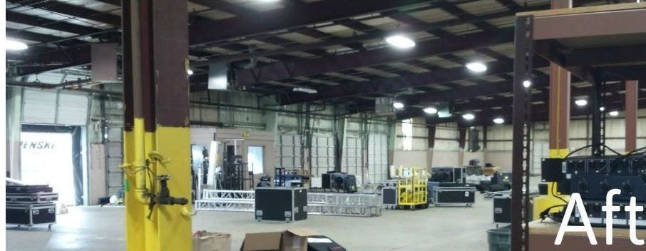 Large warehouse interior with yellow support columns, concrete floor, and stacked equipment under overhead lights