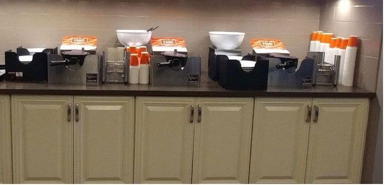 Buffet counter with coffee and juice dispensers, cups, and napkins in a kitchen or breakfast area