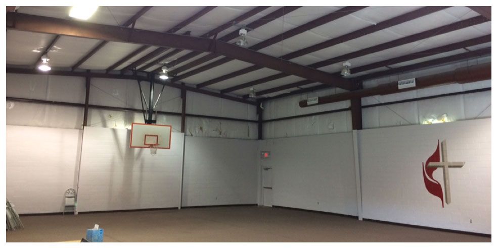 Empty indoor gym with a basketball hoop and white walls under exposed ceiling beams