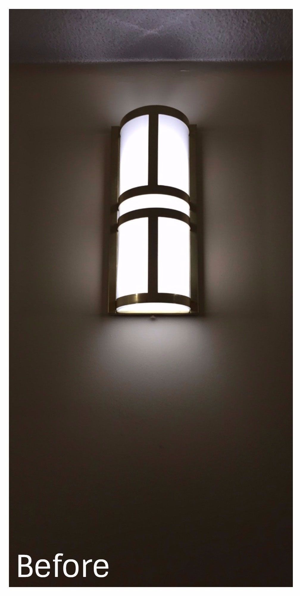 Wall-mounted cylindrical light fixture glowing softly against a dark wall.