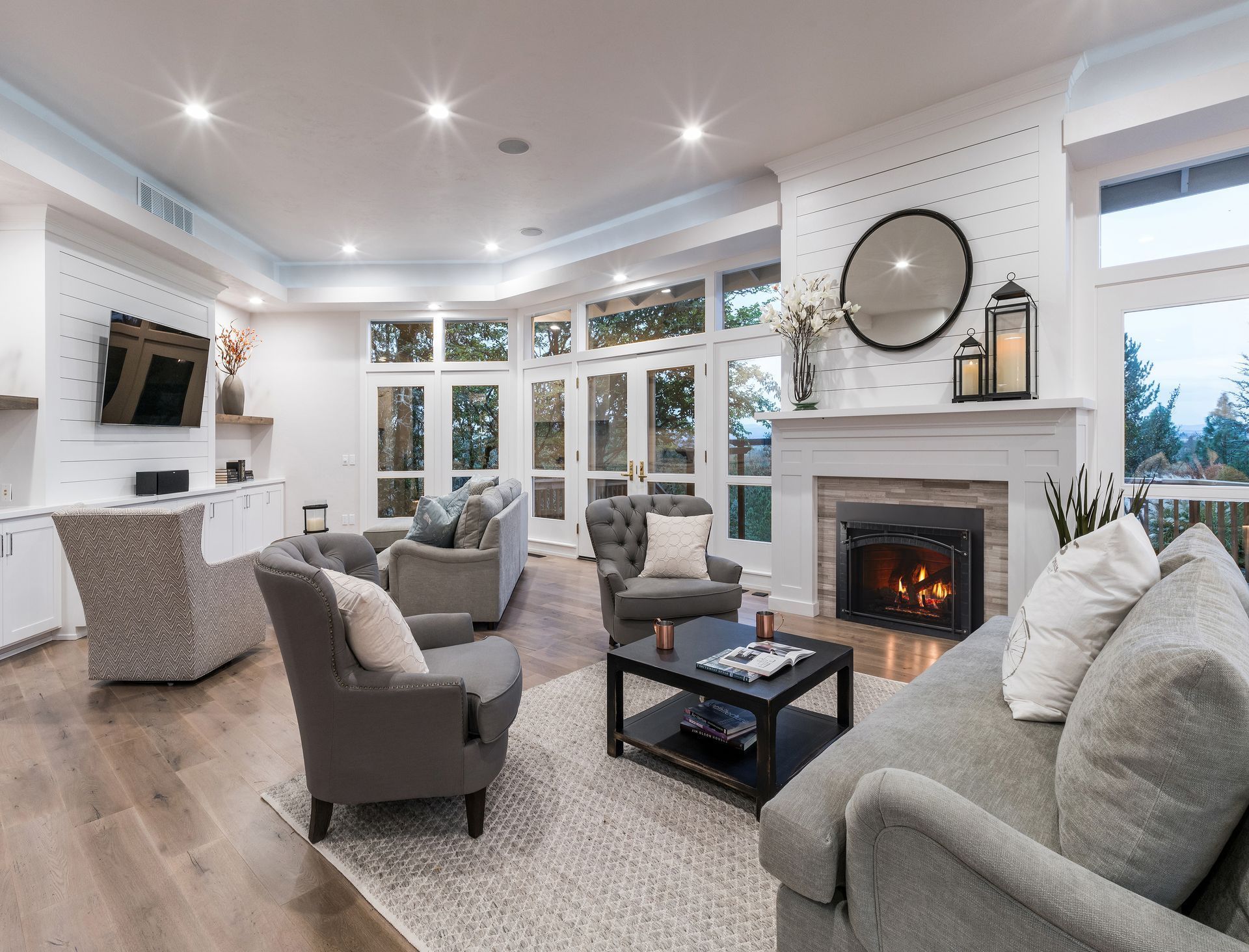 Bright living room with gray furniture, fireplace, large windows, and hardwood floors.