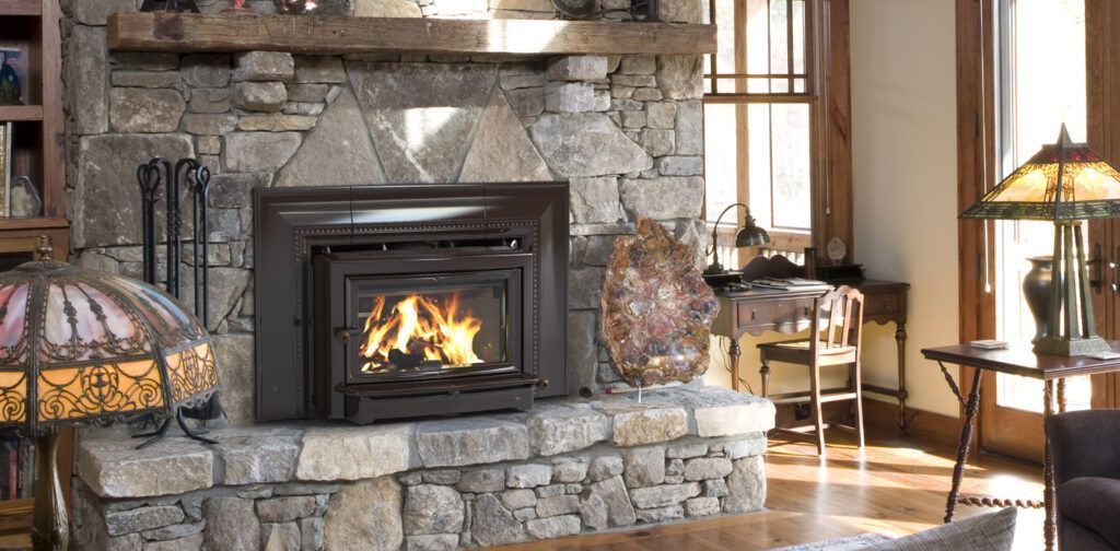 Stone fireplace with a fire burning, beside a desk and lamp, in a cozy living room