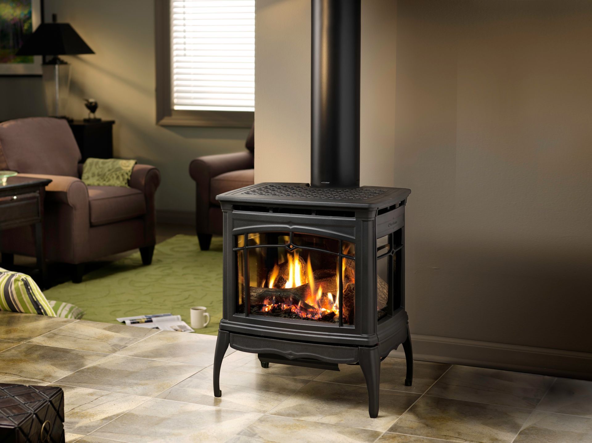Gas fireplace in living room with lit flames, black pipe, and two armchairs.