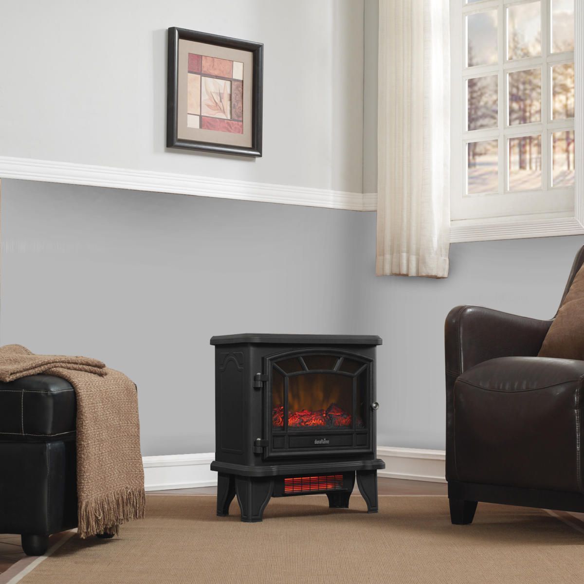 Black electric fireplace in a living room, near a chair, ottoman, and window with a painting.