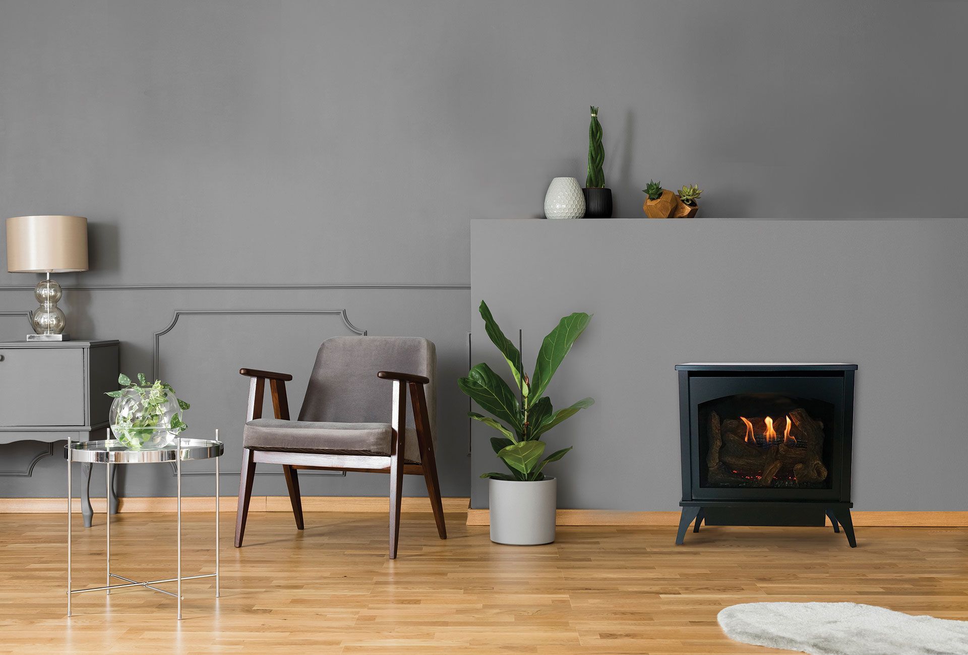 Living room with a gray wall, fireplace, armchair, side table, and plants on a wooden floor.