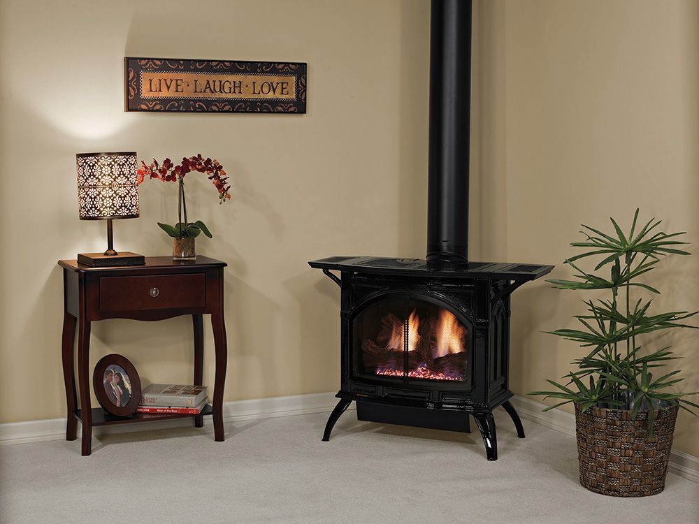 Fireplace with flames, next to a table with a lamp and vase, in a room with a plant and wall decor.