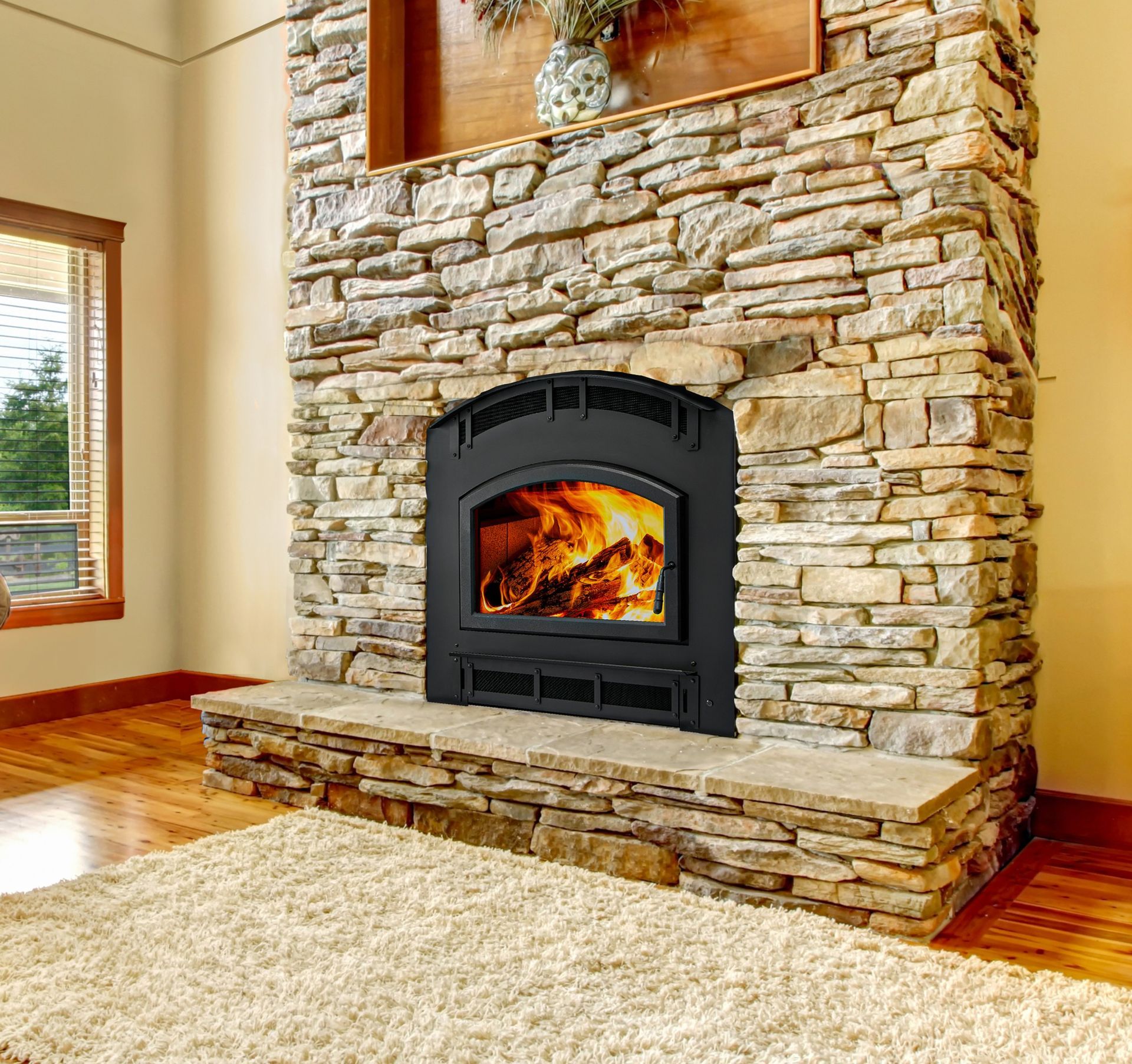 Black fireplace inset in a stone wall, flames visible. Beige rug and wood flooring in a room.