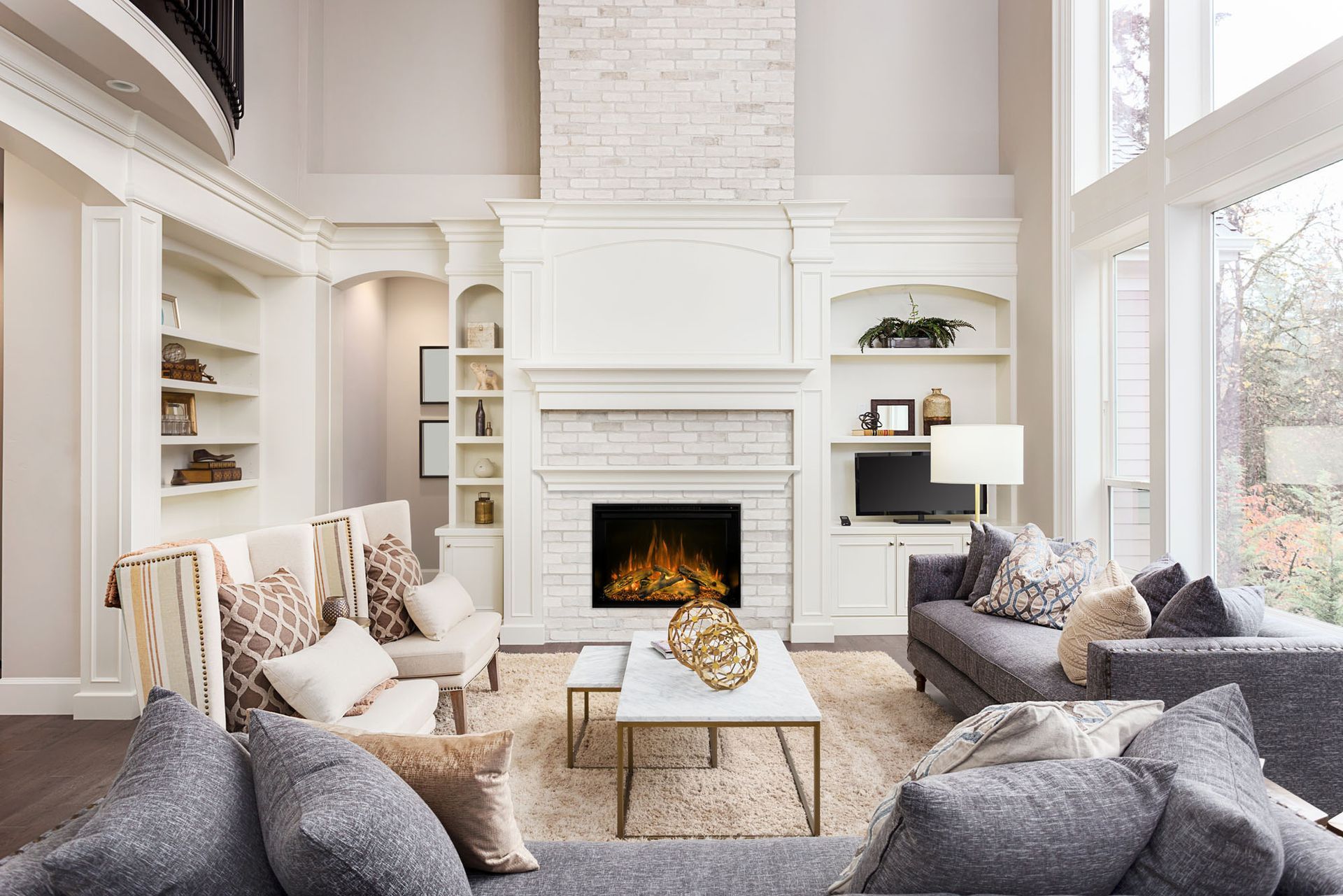 Spacious living room with white fireplace, built-in shelves, gray sofas, and large windows.