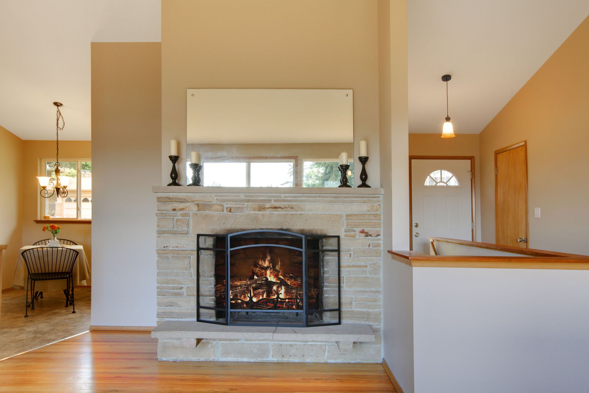 Stone fireplace with a fire burning, flanked by tall candleholders. Beige walls and hardwood floor.