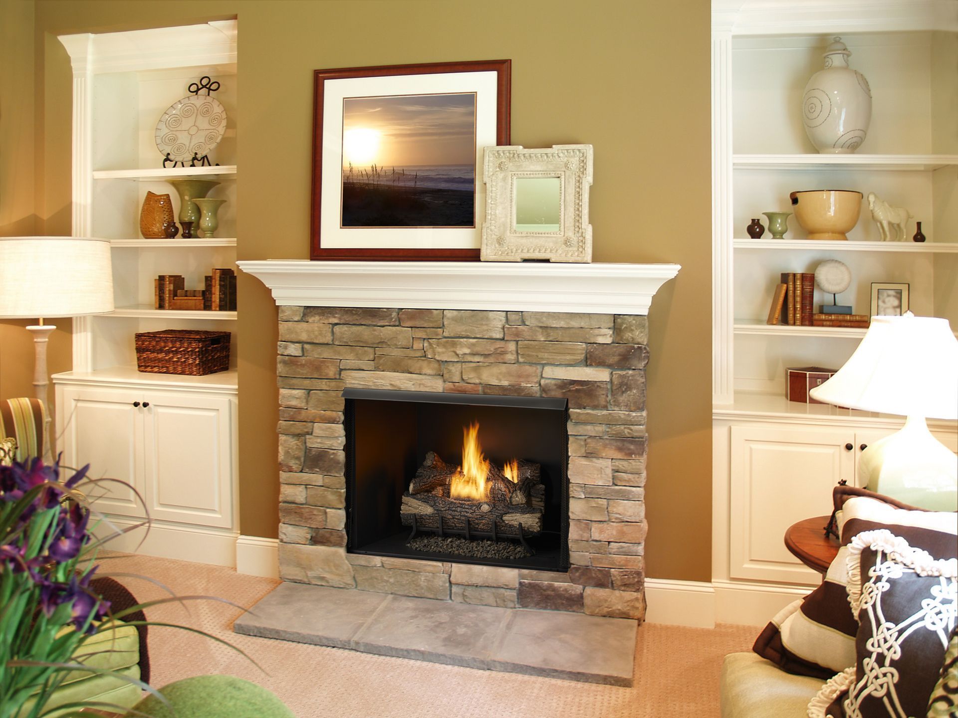 Fireplace with stone facade, flanked by white bookshelves. Artwork and decorative objects displayed.