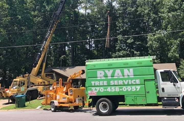 A ryan tree service truck is parked on the side of the road next to a crane.