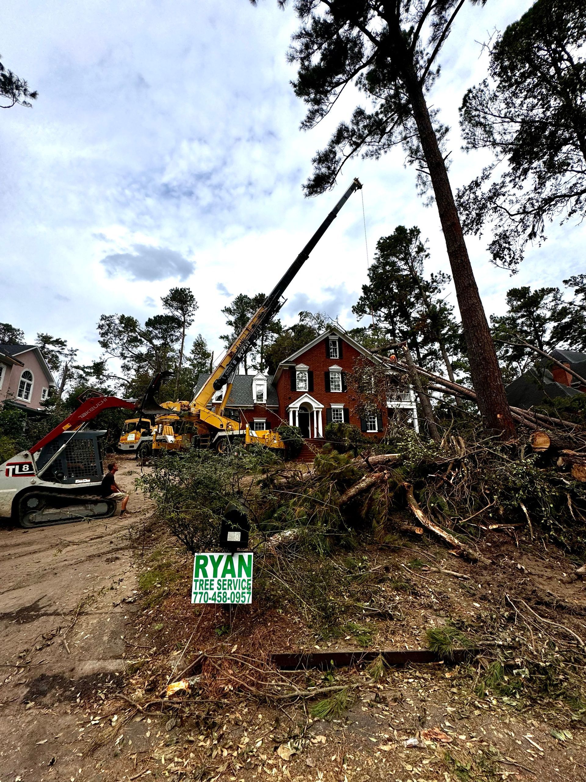 A crane is cutting down a tree in front of a house.