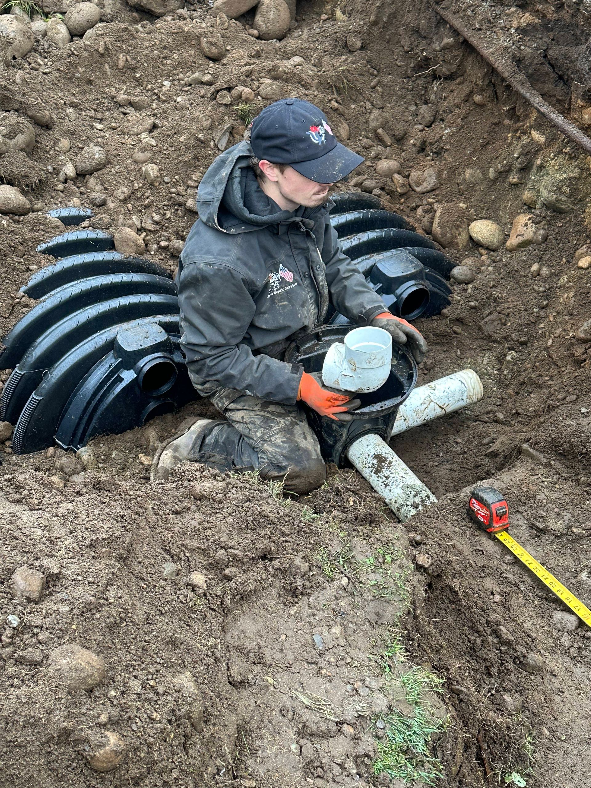 A man is kneeling in the dirt holding a pipe.